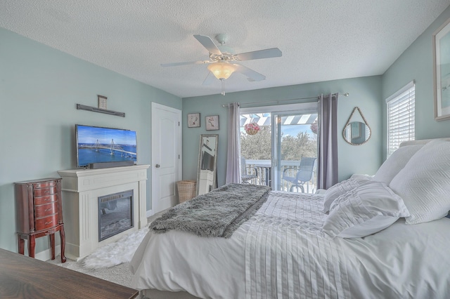 carpeted bedroom featuring a glass covered fireplace, a textured ceiling, access to exterior, and ceiling fan