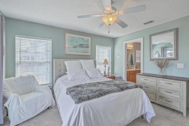 bedroom featuring visible vents, light carpet, ensuite bathroom, a textured ceiling, and a ceiling fan