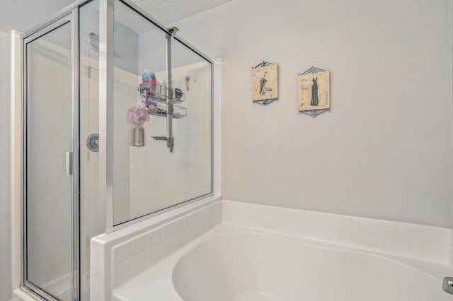 full bath with a shower stall, a textured ceiling, and a garden tub