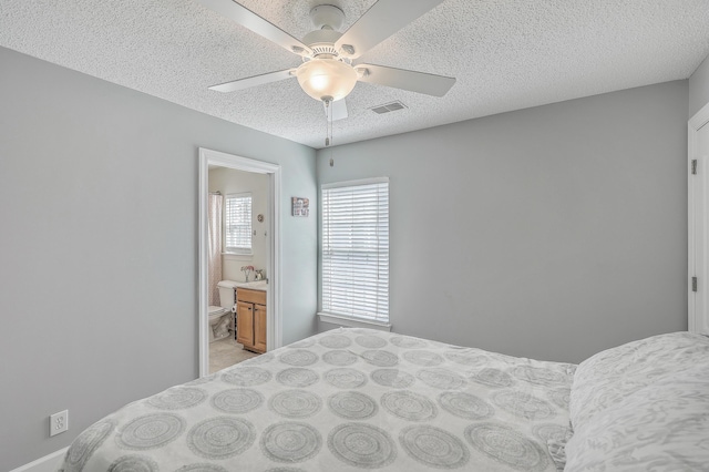 bedroom featuring visible vents, light carpet, ensuite bathroom, a textured ceiling, and a ceiling fan