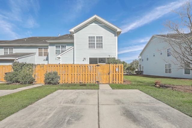 rear view of house with a gate, a lawn, and fence