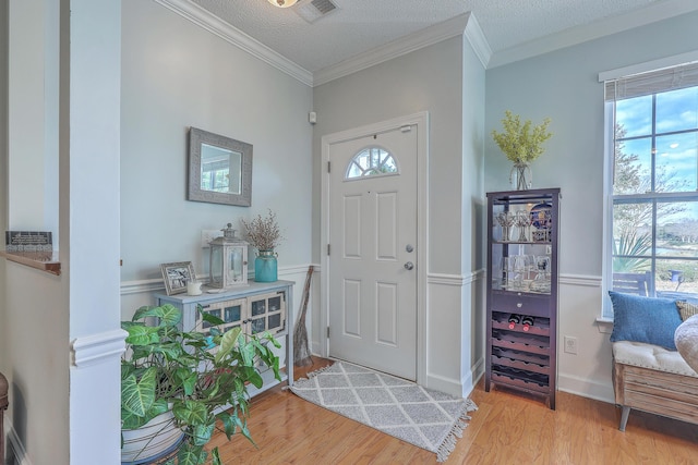 foyer entrance featuring light wood-type flooring, visible vents, and ornamental molding