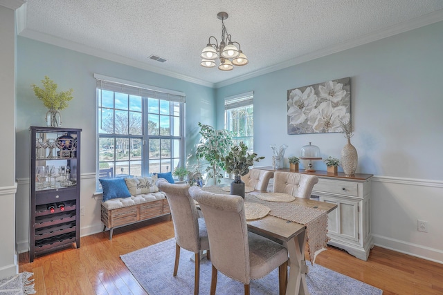 dining space featuring visible vents, an inviting chandelier, light wood-style flooring, ornamental molding, and a textured ceiling