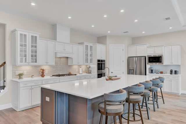 kitchen featuring an island with sink, a breakfast bar, stainless steel appliances, white cabinetry, and light wood-type flooring