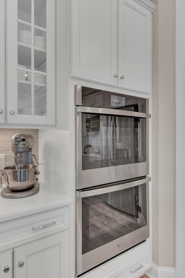 interior space featuring decorative backsplash, double oven, and white cabinets