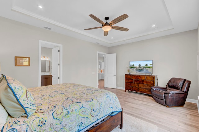 bedroom with ceiling fan, light wood-type flooring, a tray ceiling, and connected bathroom