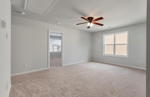 spare room with visible vents, baseboards, attic access, ceiling fan, and light colored carpet