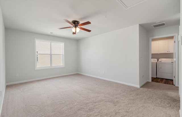 carpeted empty room with ceiling fan, attic access, visible vents, washing machine and clothes dryer, and baseboards