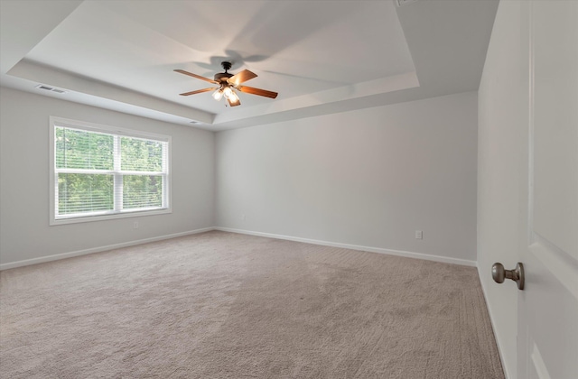 carpeted empty room featuring baseboards, ceiling fan, a tray ceiling, and visible vents
