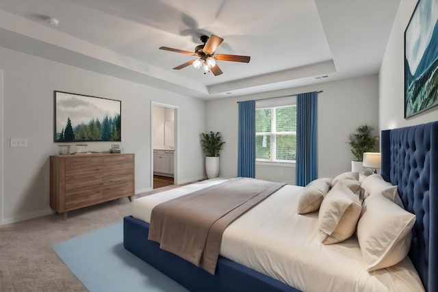 bedroom featuring a ceiling fan, light colored carpet, baseboards, ensuite bathroom, and a tray ceiling