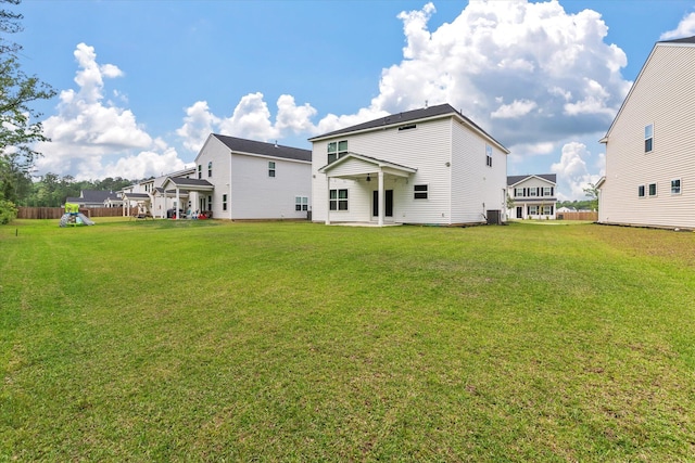 rear view of property with a lawn, a playground, a patio area, and central AC