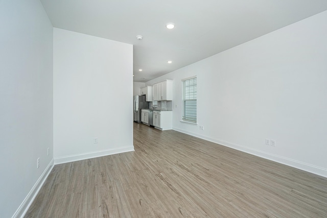 unfurnished living room with recessed lighting, baseboards, and light wood-type flooring