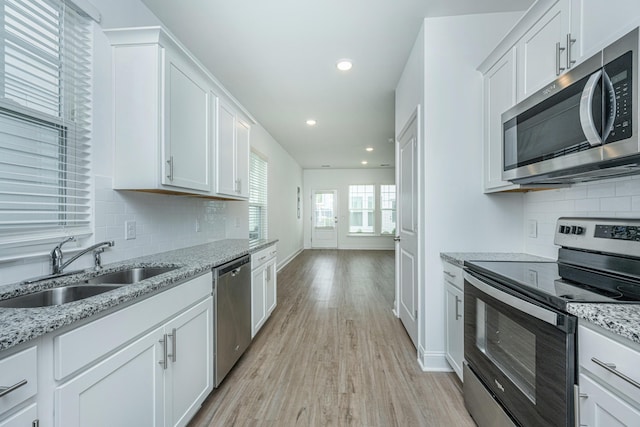 kitchen featuring a sink, white cabinets, light wood-style floors, appliances with stainless steel finishes, and backsplash