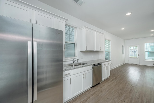 kitchen featuring visible vents, a sink, stainless steel appliances, white cabinetry, and light wood-type flooring