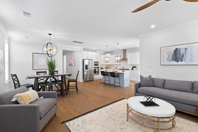 living room with crown molding, ceiling fan with notable chandelier, and light wood-type flooring