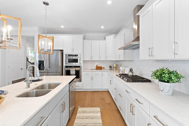 kitchen with sink, wall chimney exhaust hood, stainless steel appliances, decorative light fixtures, and white cabinets