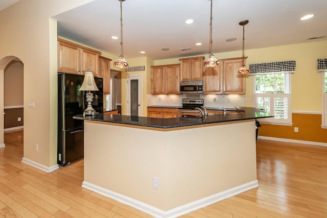 kitchen featuring stainless steel appliances, light wood-type flooring, tasteful backsplash, a sink, and baseboards