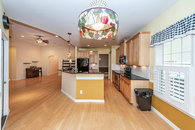 kitchen with stainless steel appliances, dark countertops, light wood-style flooring, arched walkways, and decorative backsplash