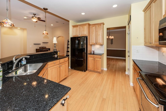 kitchen featuring freestanding refrigerator, a sink, stainless steel range with electric stovetop, light brown cabinets, and arched walkways