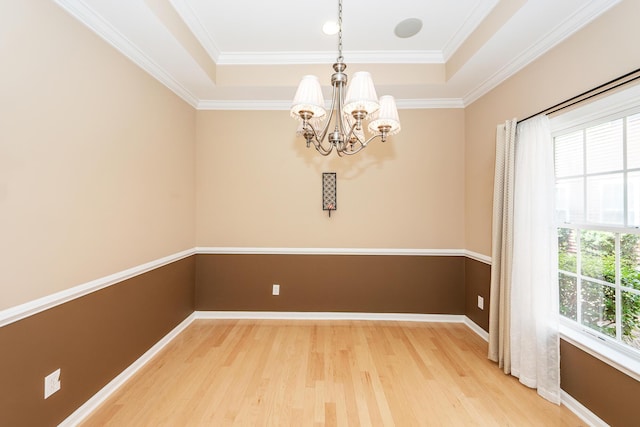 empty room featuring light wood-style flooring, a tray ceiling, a chandelier, baseboards, and ornamental molding