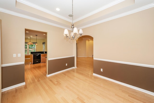 spare room featuring a tray ceiling, arched walkways, light wood-style floors, a chandelier, and ornamental molding