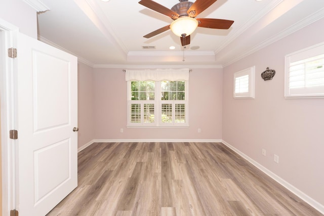 empty room featuring a raised ceiling, healthy amount of natural light, light wood-style flooring, ceiling fan, and crown molding