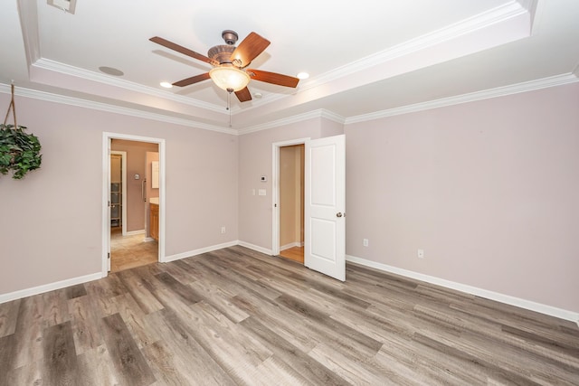 unfurnished bedroom featuring a raised ceiling, light wood-style flooring, crown molding, baseboards, and ceiling fan