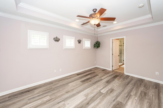 empty room featuring a tray ceiling, wood finished floors, ceiling fan, crown molding, and baseboards