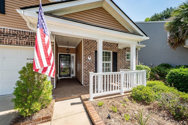 doorway to property featuring brick siding, a porch, and an attached garage