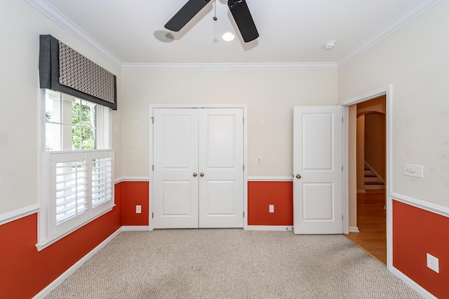 unfurnished bedroom with crown molding, light colored carpet, a closet, baseboards, and ceiling fan