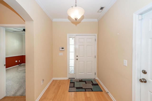 entryway with arched walkways, light wood-style floors, baseboards, and crown molding
