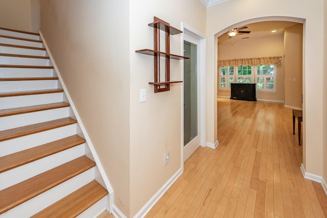 hallway with arched walkways, light wood-style floors, stairway, and baseboards