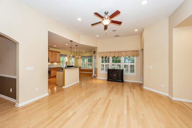 unfurnished living room featuring a ceiling fan, light wood-style floors, arched walkways, recessed lighting, and baseboards