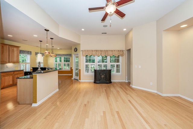 kitchen featuring open floor plan, light wood-style flooring, dark countertops, ceiling fan, and decorative light fixtures