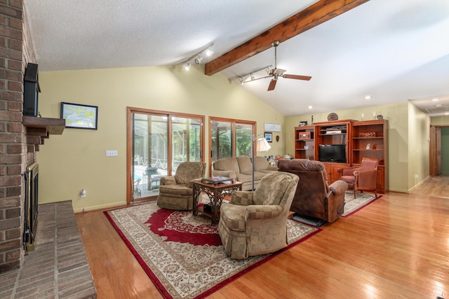 living room featuring hardwood / wood-style flooring, ceiling fan, lofted ceiling with beams, a textured ceiling, and a brick fireplace