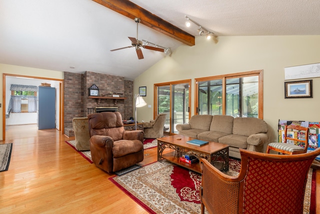 living room featuring ceiling fan, a fireplace, lofted ceiling with beams, a textured ceiling, and light wood-type flooring