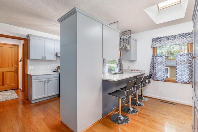 kitchen featuring sink, gray cabinets, hanging light fixtures, a skylight, and light hardwood / wood-style floors