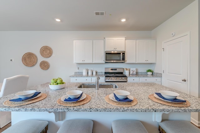 kitchen with sink, light stone counters, a center island with sink, white cabinets, and appliances with stainless steel finishes