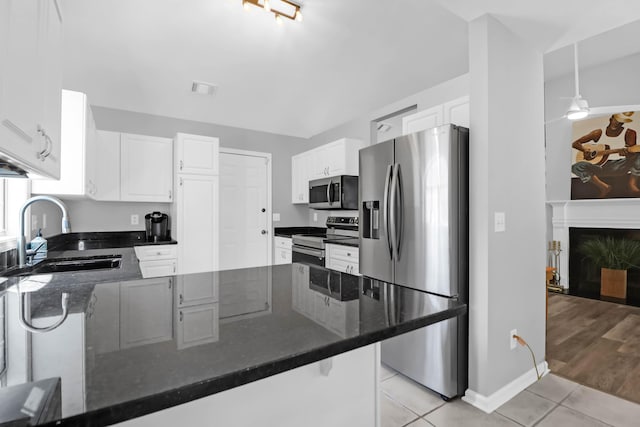 kitchen featuring a peninsula, white cabinets, a sink, light tile patterned floors, and stainless steel appliances