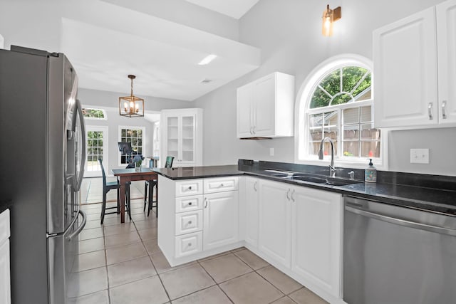 kitchen with white cabinets, dark countertops, appliances with stainless steel finishes, a sink, and a peninsula