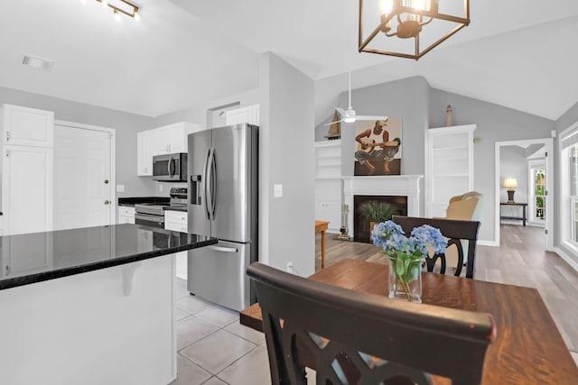 dining area with built in features, a ceiling fan, a fireplace with flush hearth, lofted ceiling, and visible vents