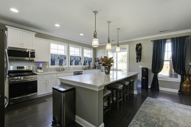 kitchen with stainless steel appliances, sink, decorative light fixtures, white cabinets, and a center island