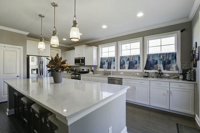 kitchen featuring light stone countertops, a center island, stainless steel appliances, pendant lighting, and white cabinets