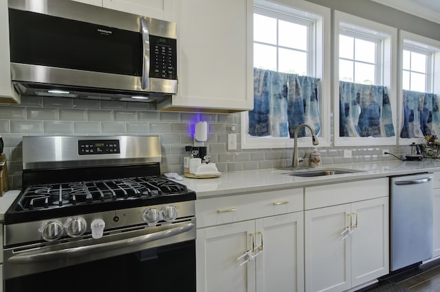 kitchen featuring light stone countertops, a wealth of natural light, stainless steel appliances, sink, and white cabinetry