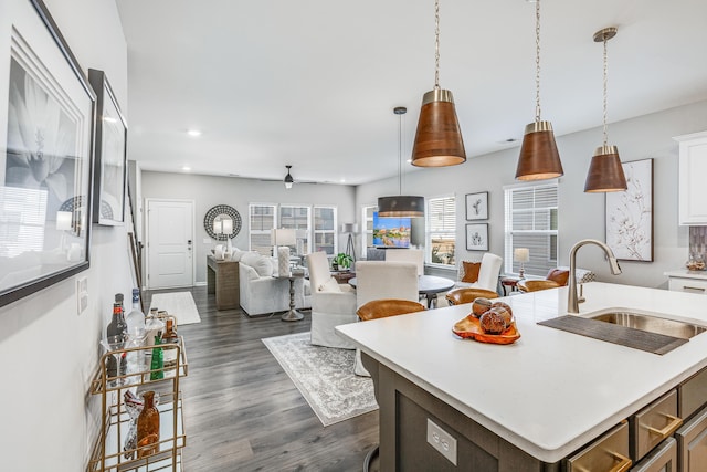 kitchen featuring ceiling fan, a kitchen island with sink, sink, pendant lighting, and white cabinetry