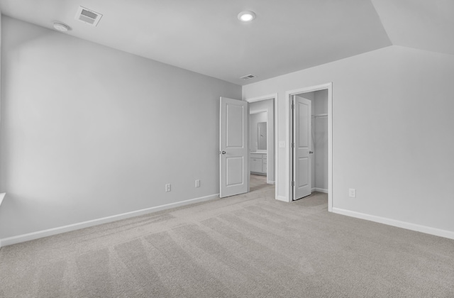 unfurnished bedroom with light colored carpet, lofted ceiling, and a walk in closet