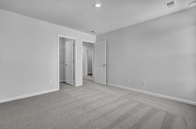 unfurnished bedroom featuring light colored carpet and a walk in closet