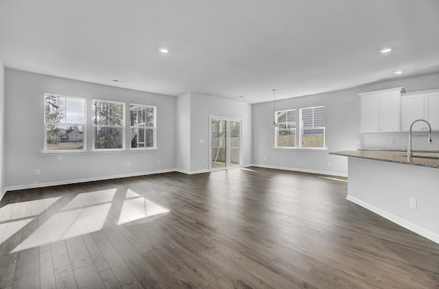 unfurnished living room with dark wood-type flooring, sink, and a wealth of natural light