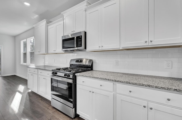 kitchen with appliances with stainless steel finishes, white cabinetry, dark hardwood / wood-style floors, light stone counters, and tasteful backsplash