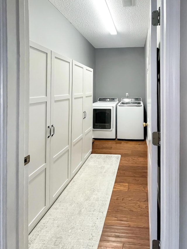 laundry room with laundry area, independent washer and dryer, a textured ceiling, and wood finished floors